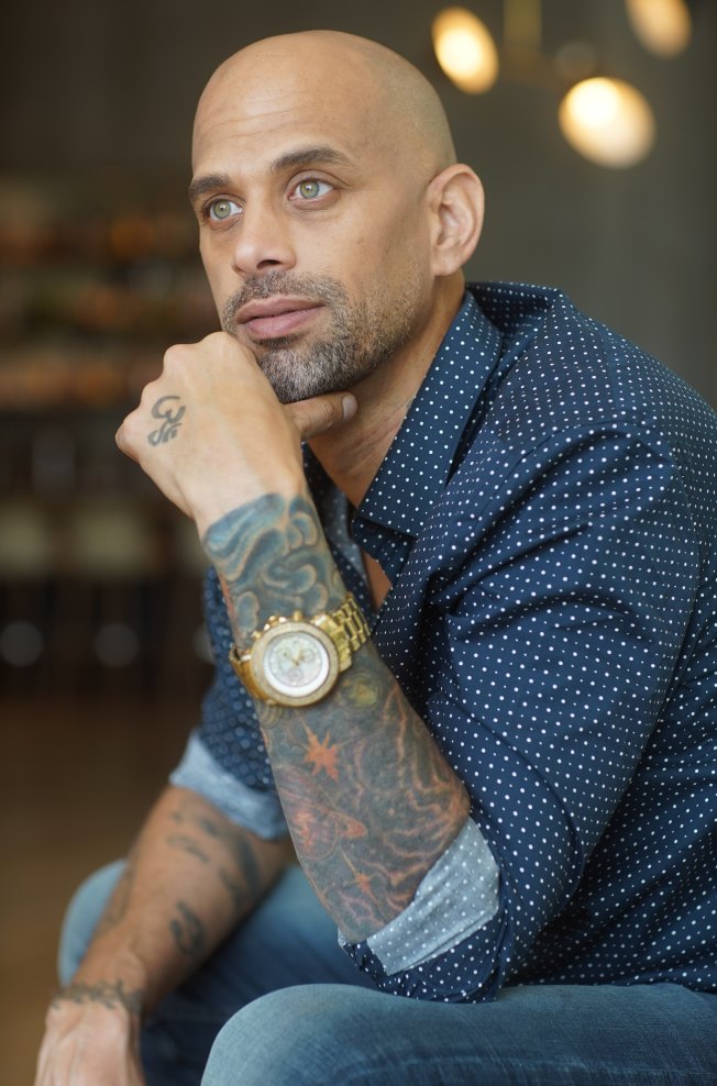 Marc Marcel seated, chin resting on his tattooed hand